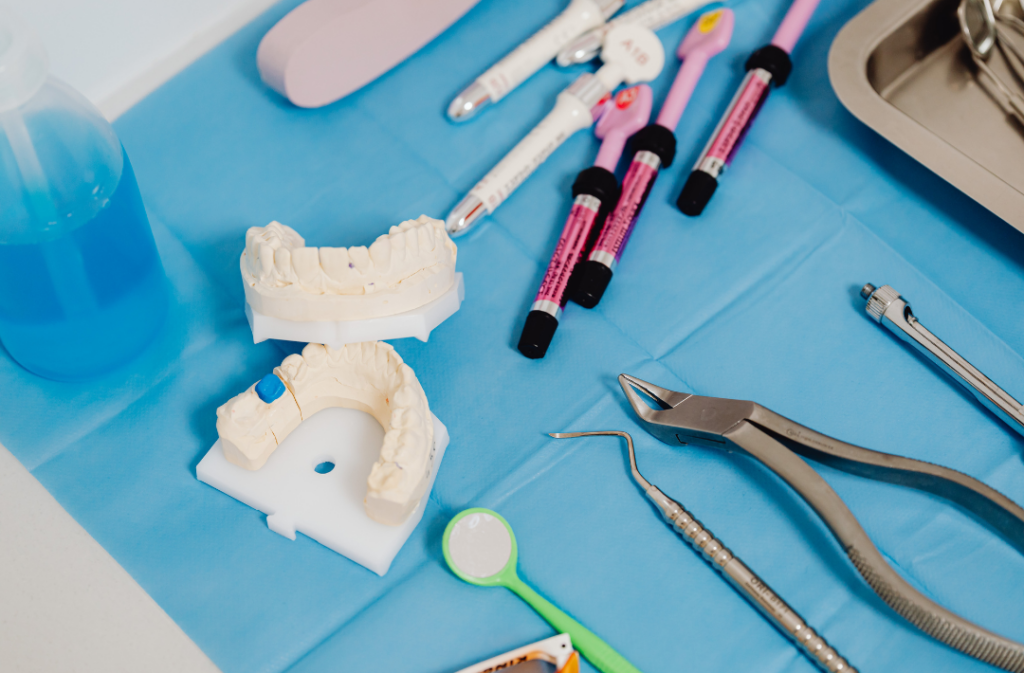 A close-up, high-angle view of a neat dental workspace with various tools laid out on a blue bib. It features a plaster dental cast model, various colorful medical instruments, a small dental mirror, and metal pliers.