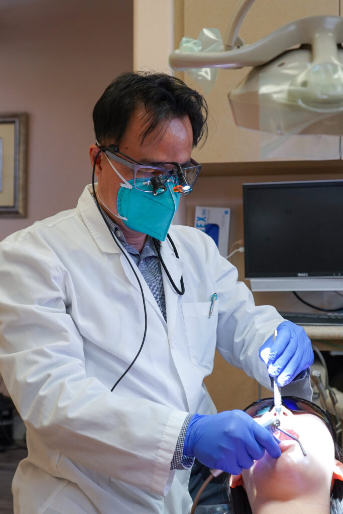 Dr. Thuc Luu wearing a surgical mask, protective loupes, and blue gloves while performing a precise dental extraction procedure on a patient at Fairview Dental.